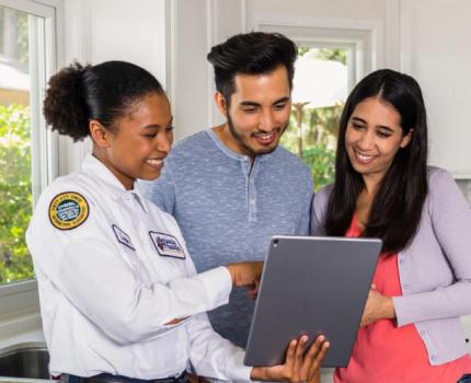 Plumbing professional showing a tablet to a couple in their kitchen.