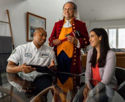 Actor dressed as Benjamin Franklin holding a wrench and smiling.